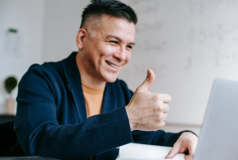 Smiling man giving a thumbs up at his laptop
