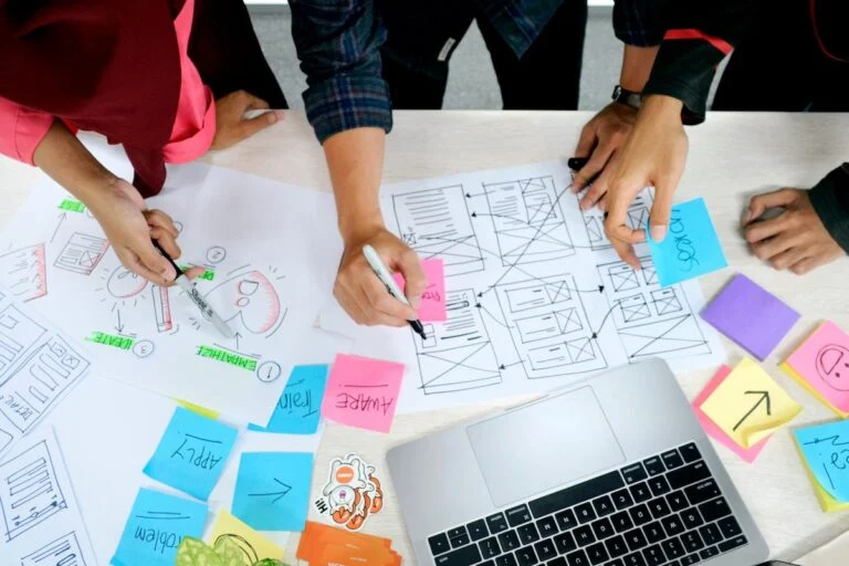 Team sketching website wireframes on paper with sticky notes around a laptop