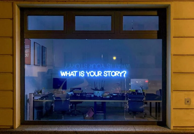 Neon window sign reading What is your story