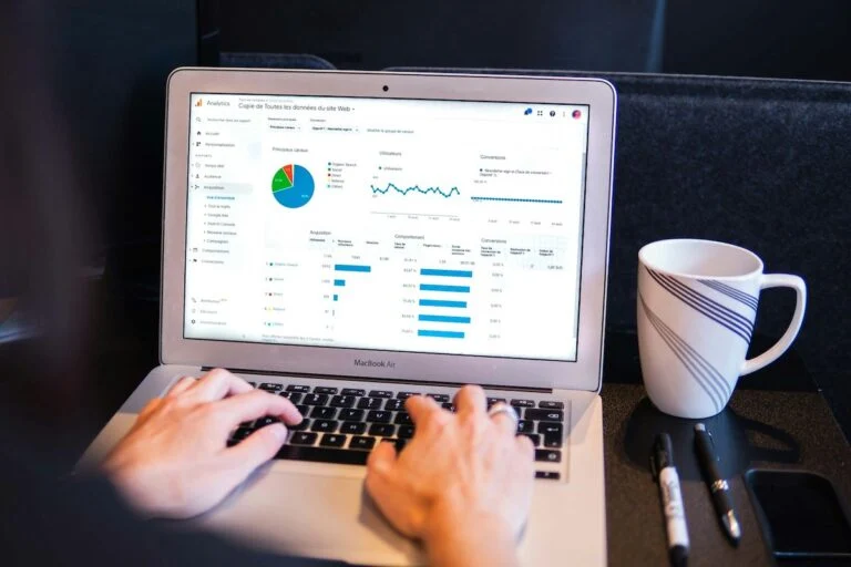 Hands typing on a laptop showing analytics charts, beside a mug