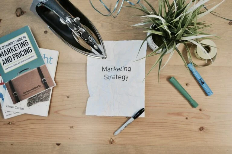 Desk with a marketing and pricing book, pens, a plant and a page headed Marketing Strategy