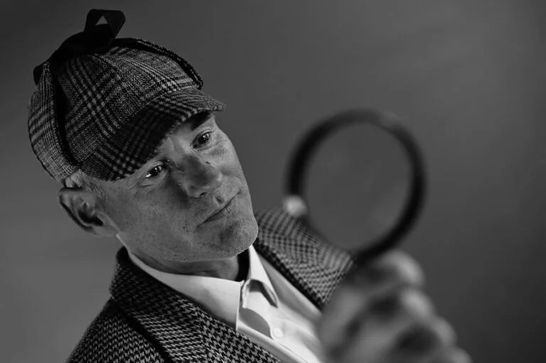 Man in a deerstalker hat holding a magnifying glass