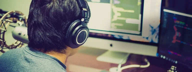 Person in headphones working at a desktop computer with code on the screen