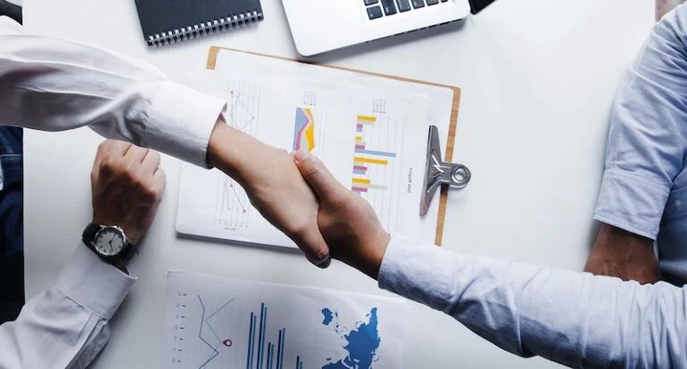Two people shaking hands over printed charts on a table