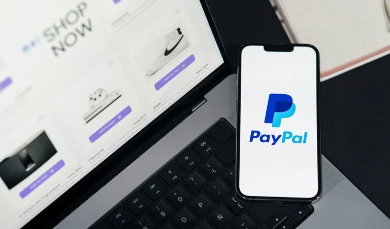 Phone showing the PayPal logo beside a laptop open to an online store