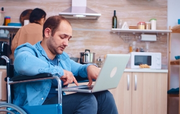 A man using a laptop from his wheelchair in his kitchen
